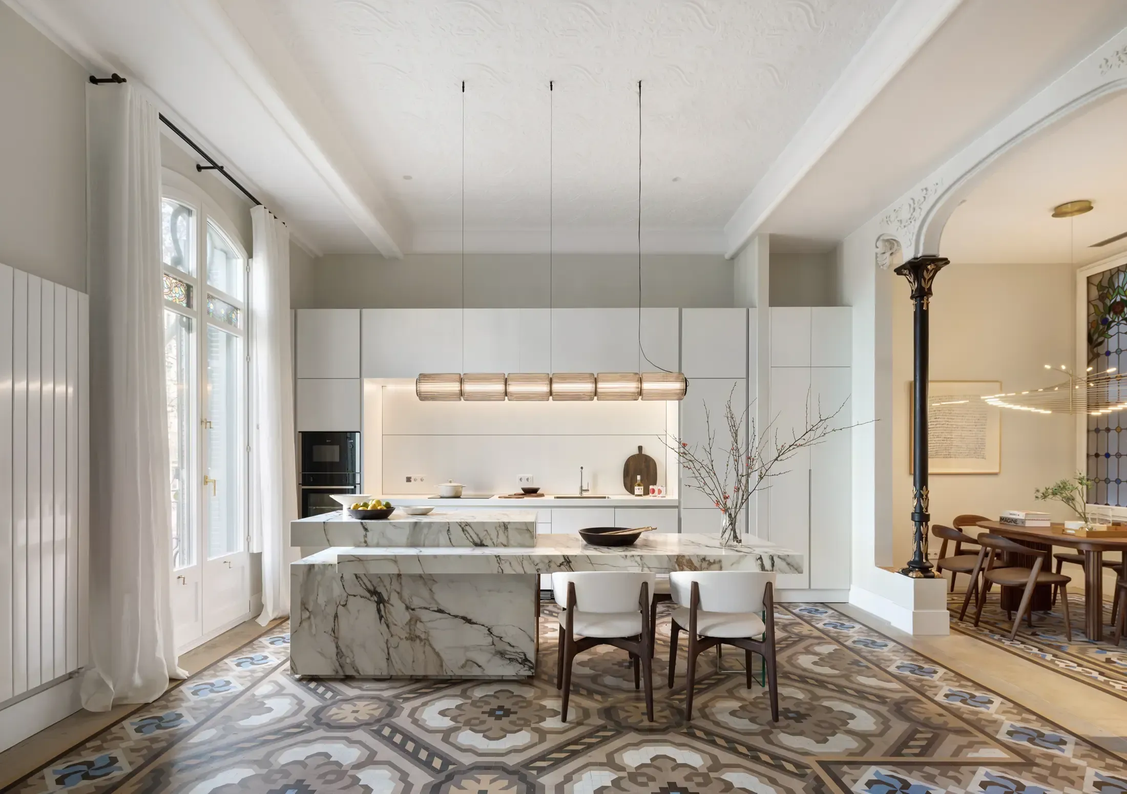 Open-plan luxury kitchen by LUV Studio with marble island, geometric floor tiles and natural light through arched windows.